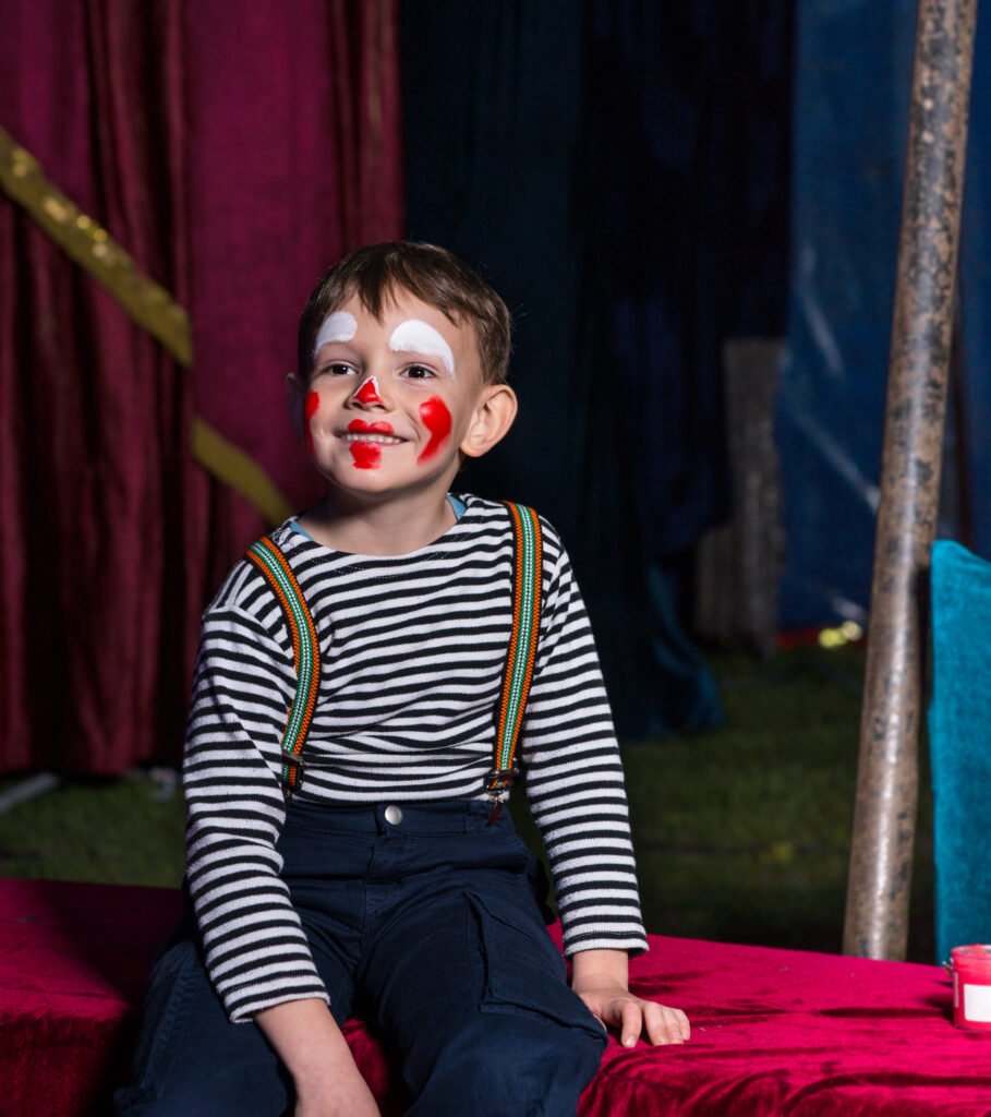 Stages happy boy with clown make up sitting on a stage